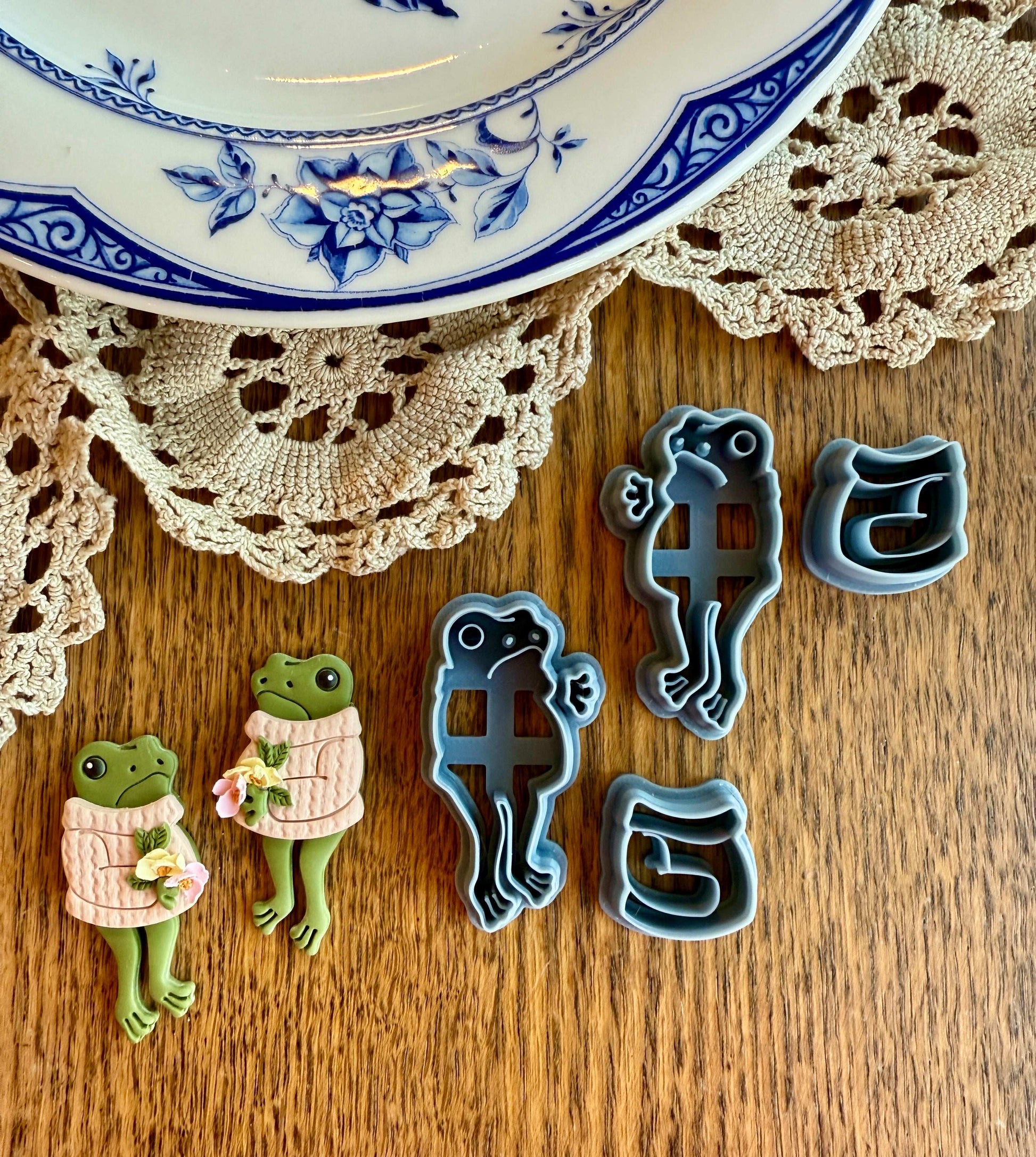 Frog in sweater clay cutters on wooden table with lace doilies.